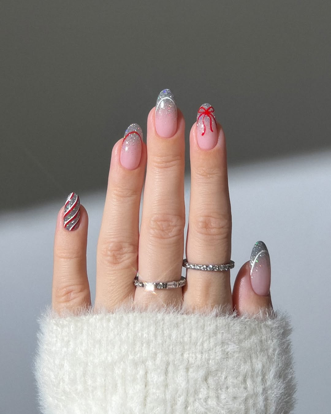 Soft pink nails with silver glitter French tips and red bow accents