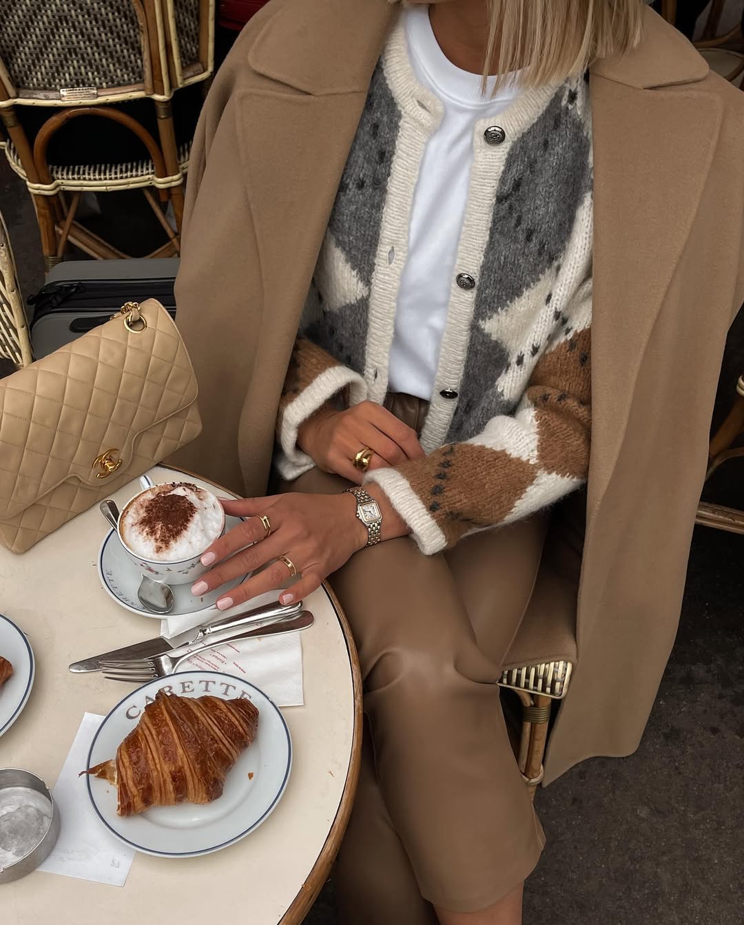Patterned cardigan under a camel coat with leather trousers.