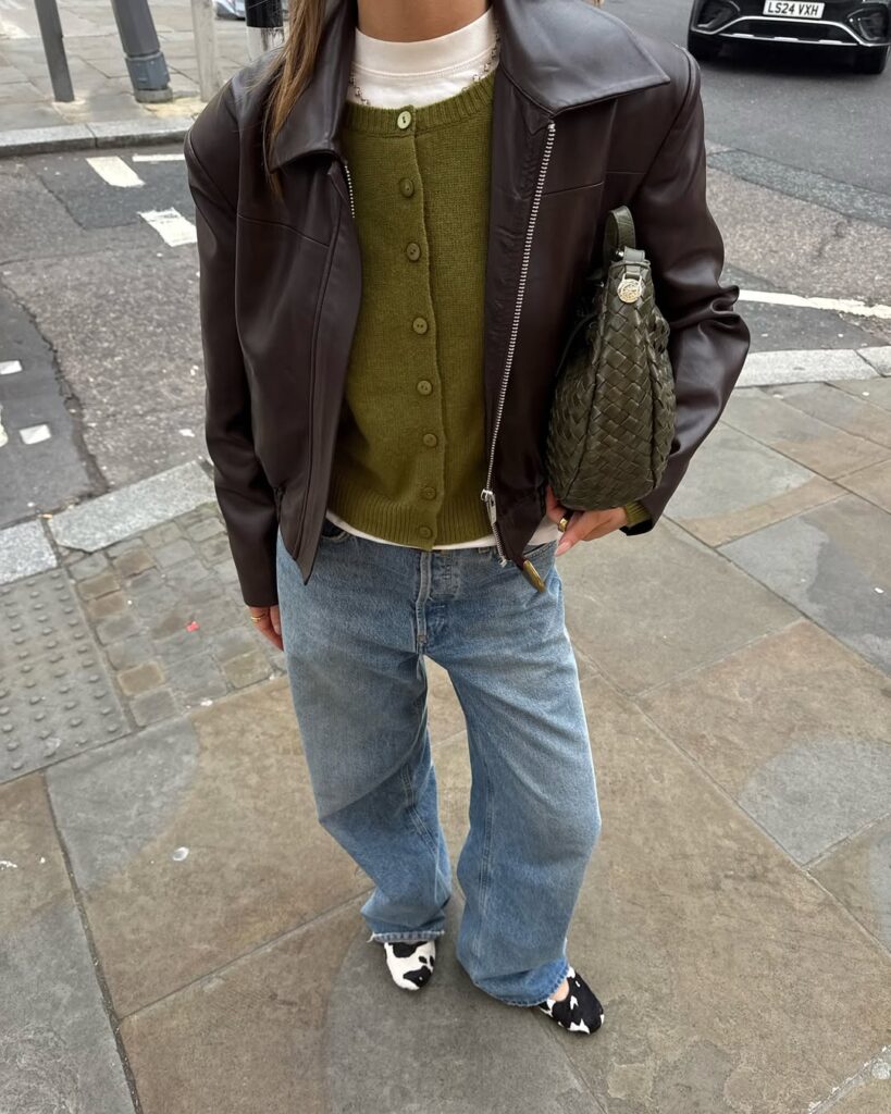 Olive cardigan layered under a leather jacket with wide-leg jeans.