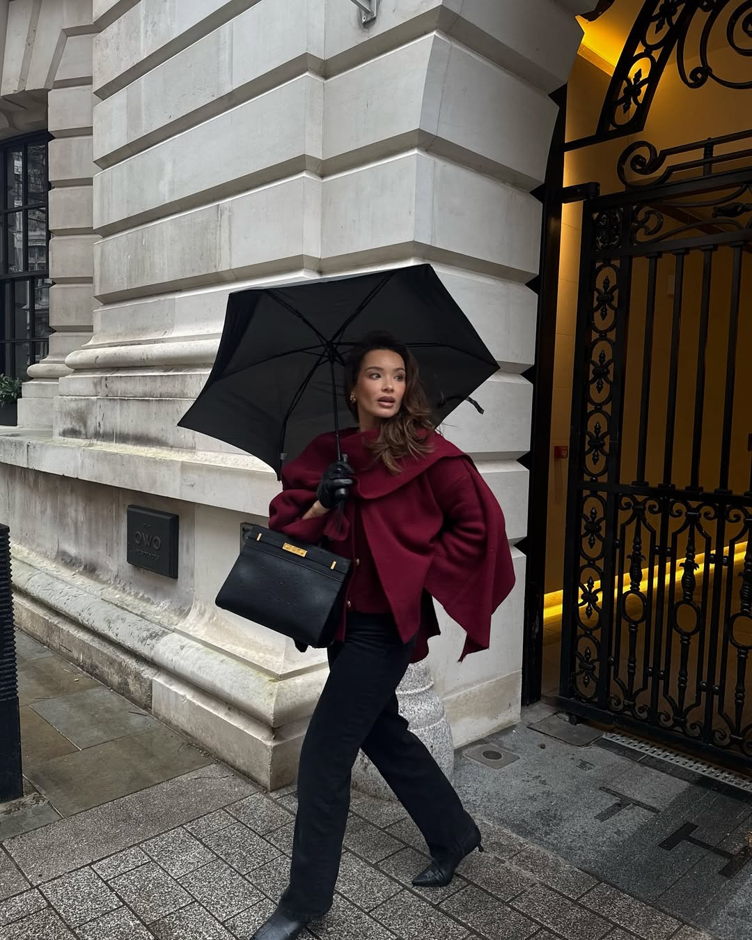 Woman in a burgundy cape coat with black trousers, gloves, and boots.