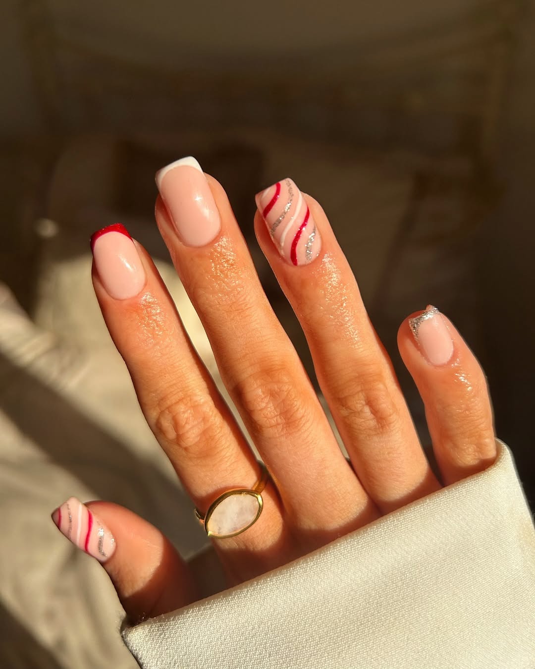 Nude base nails with swirling red and silver candy cane designs and clean French tips.