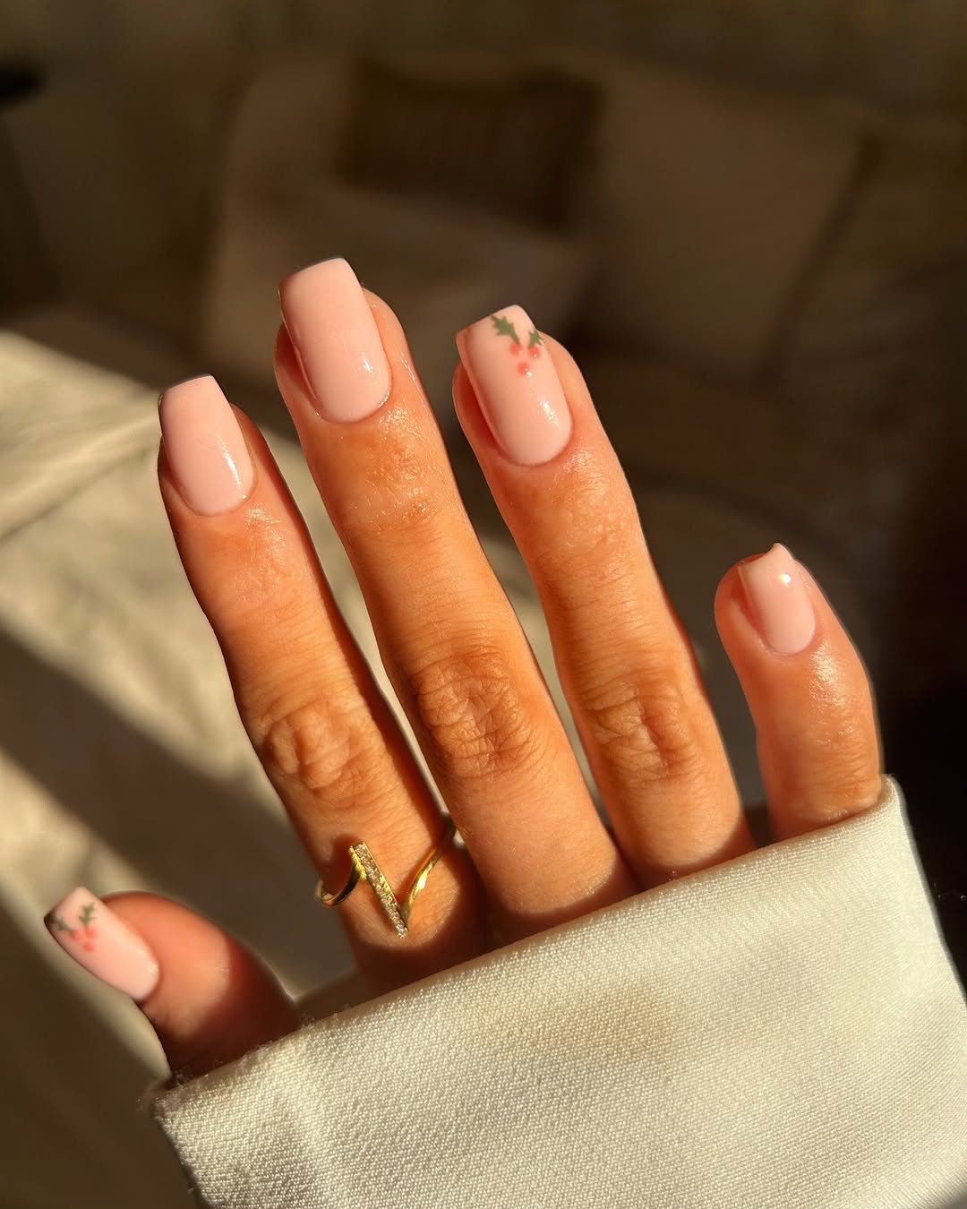 Nude pink nails with a single accent nail featuring a small holly sprig.