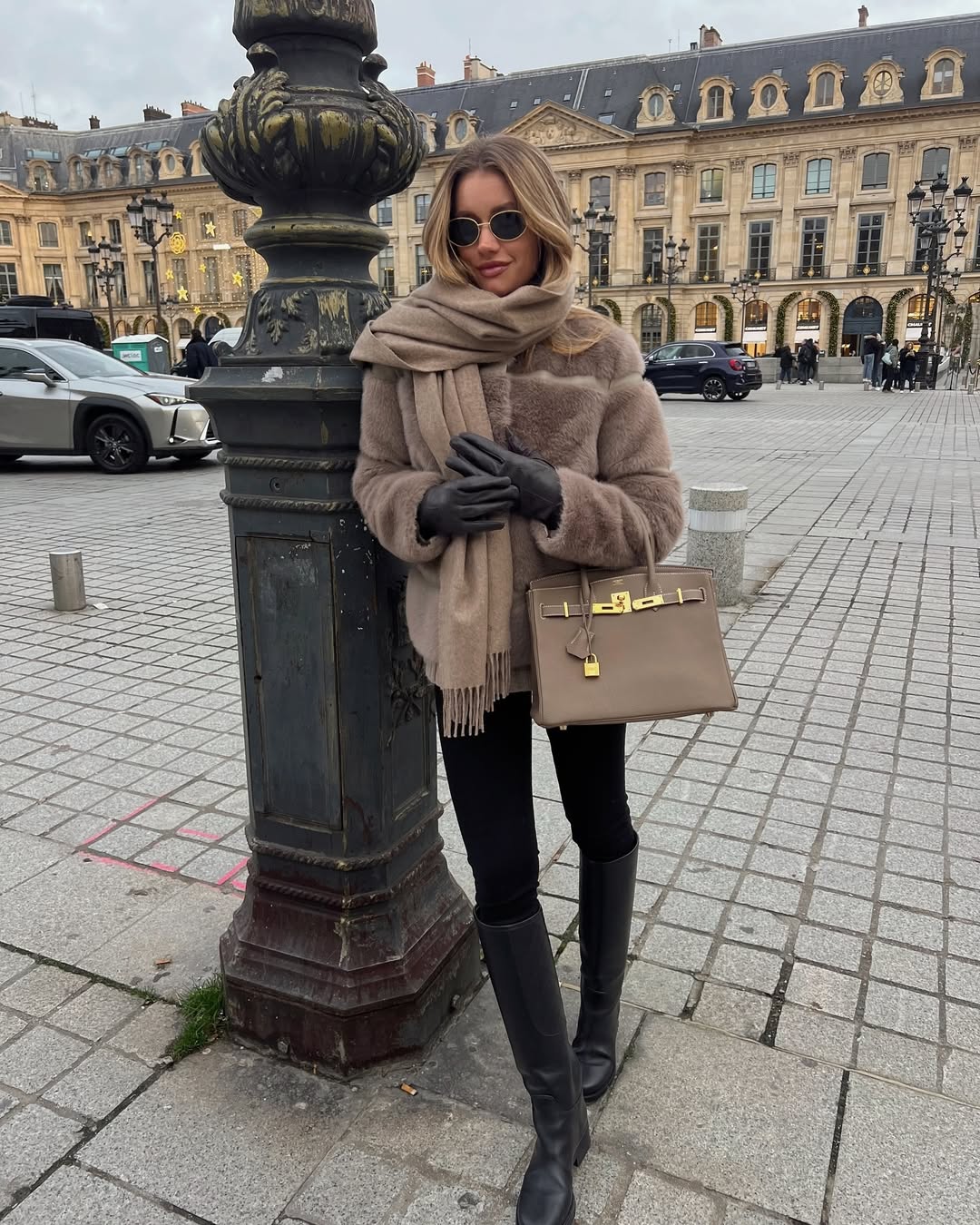 Woman in a faux fur coat with taupe scarf and black leather boots.