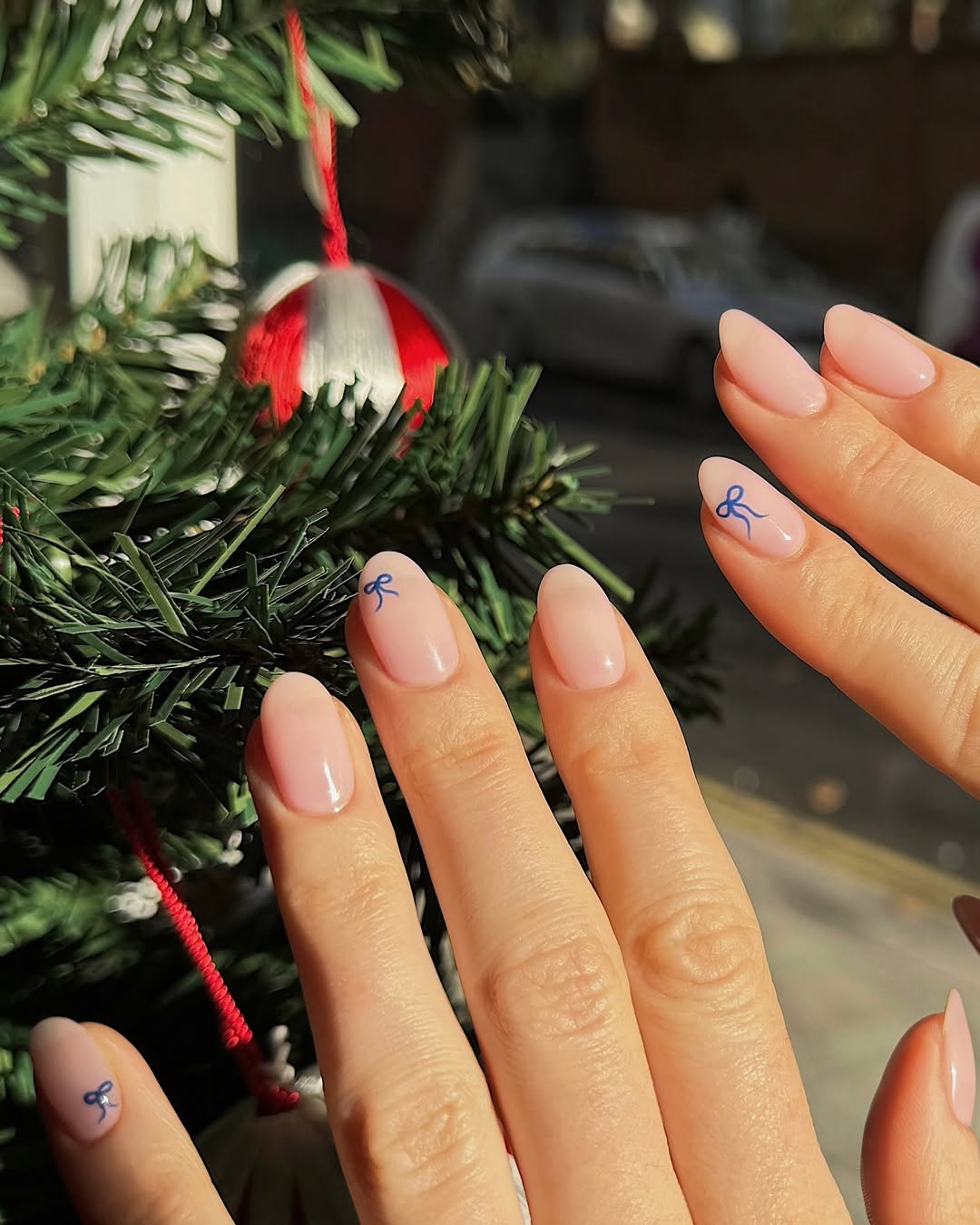 Clean nude nails adorned with small, hand-painted blue bows on select nails.