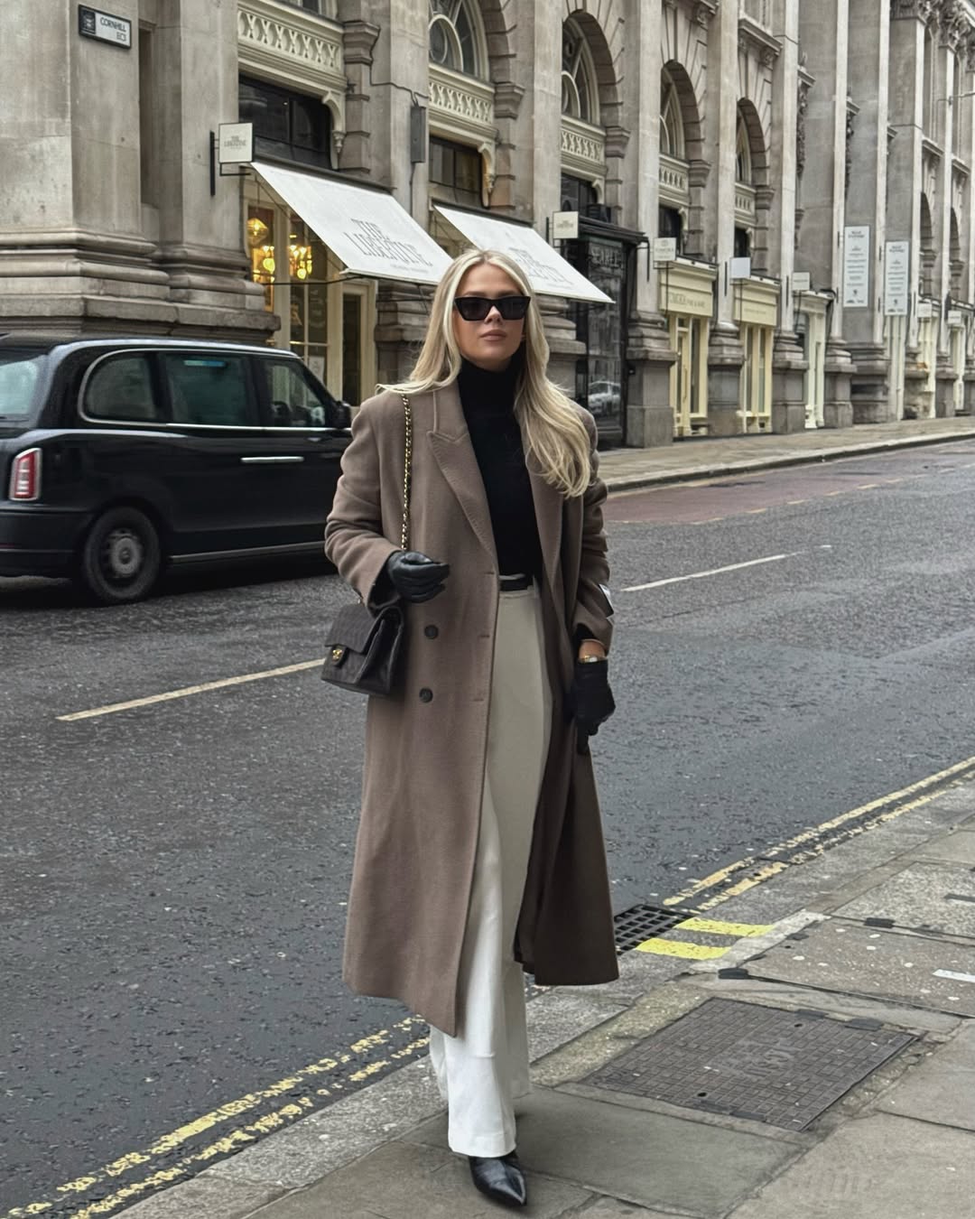 Woman wearing a taupe long coat over black and ivory layers with black boots.