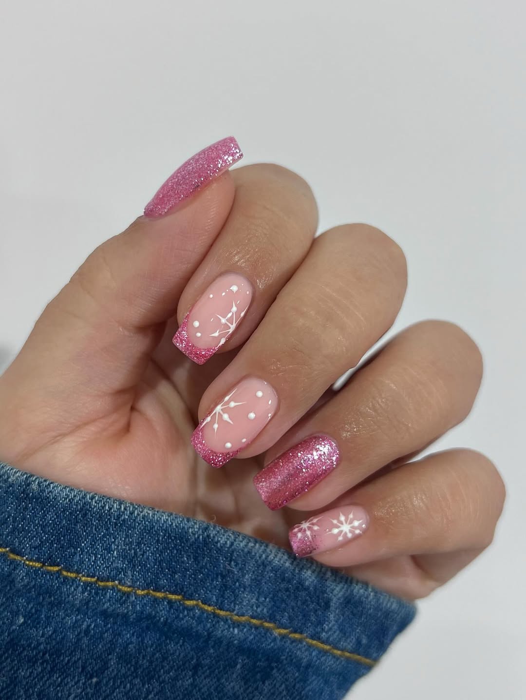 Nude nails with bright pink glitter tips, snowflakes, and dots