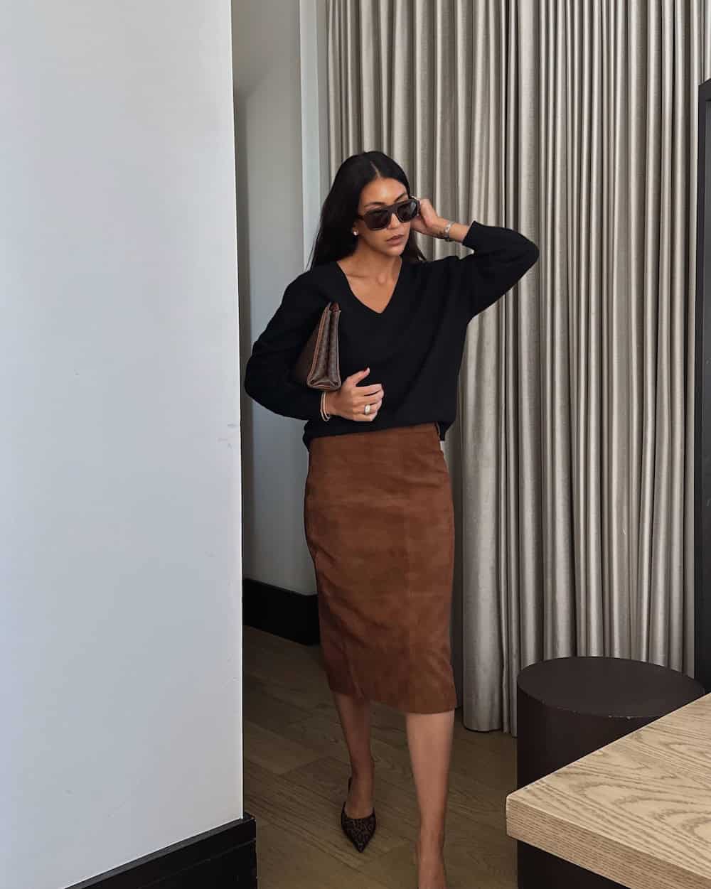 a woman wearing a brown suede pencil skirt and a black v neck sweater with black pumps