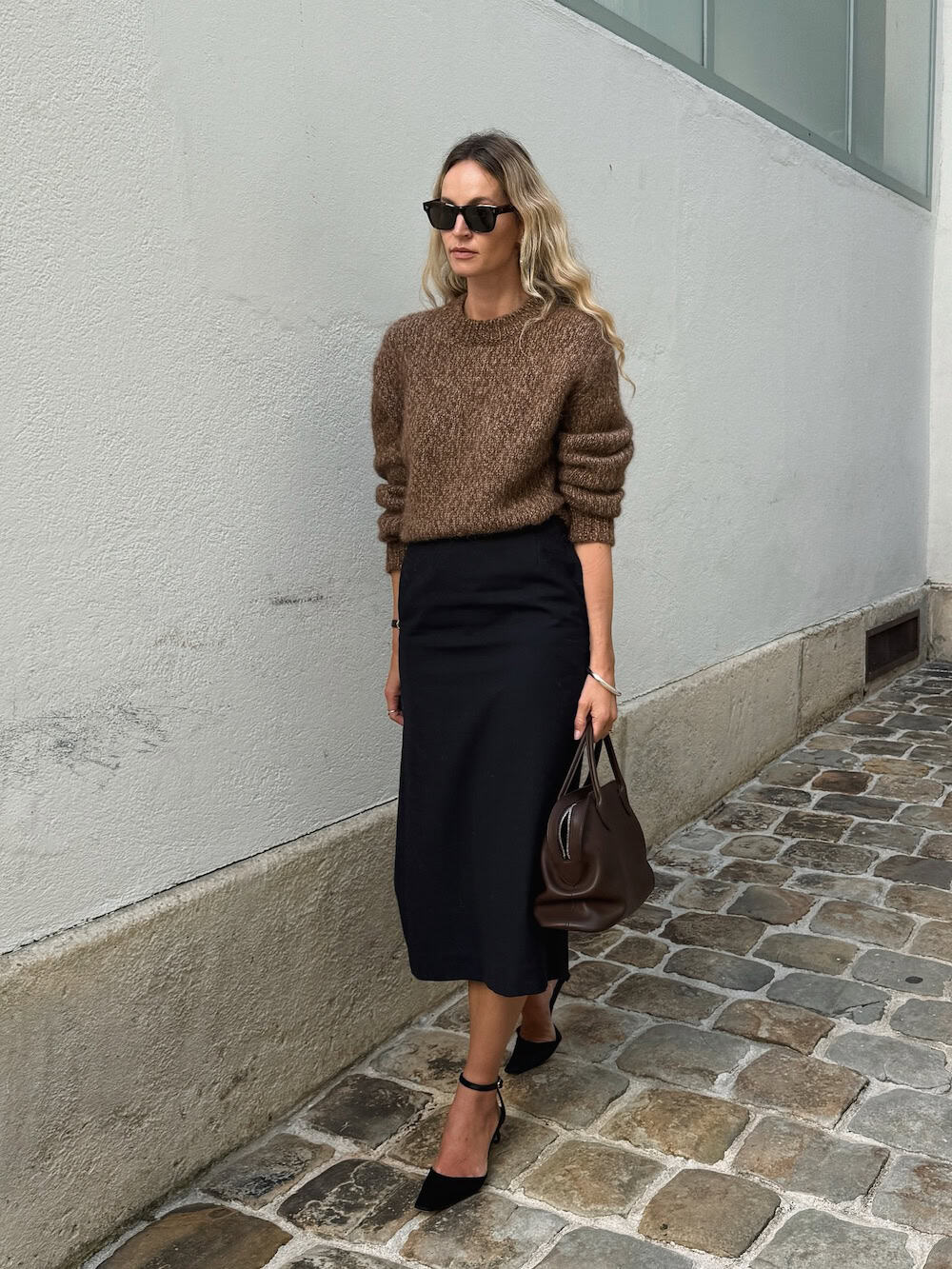 a woman wearing a black pencil skirt, a brown knit crewneck, and black heels