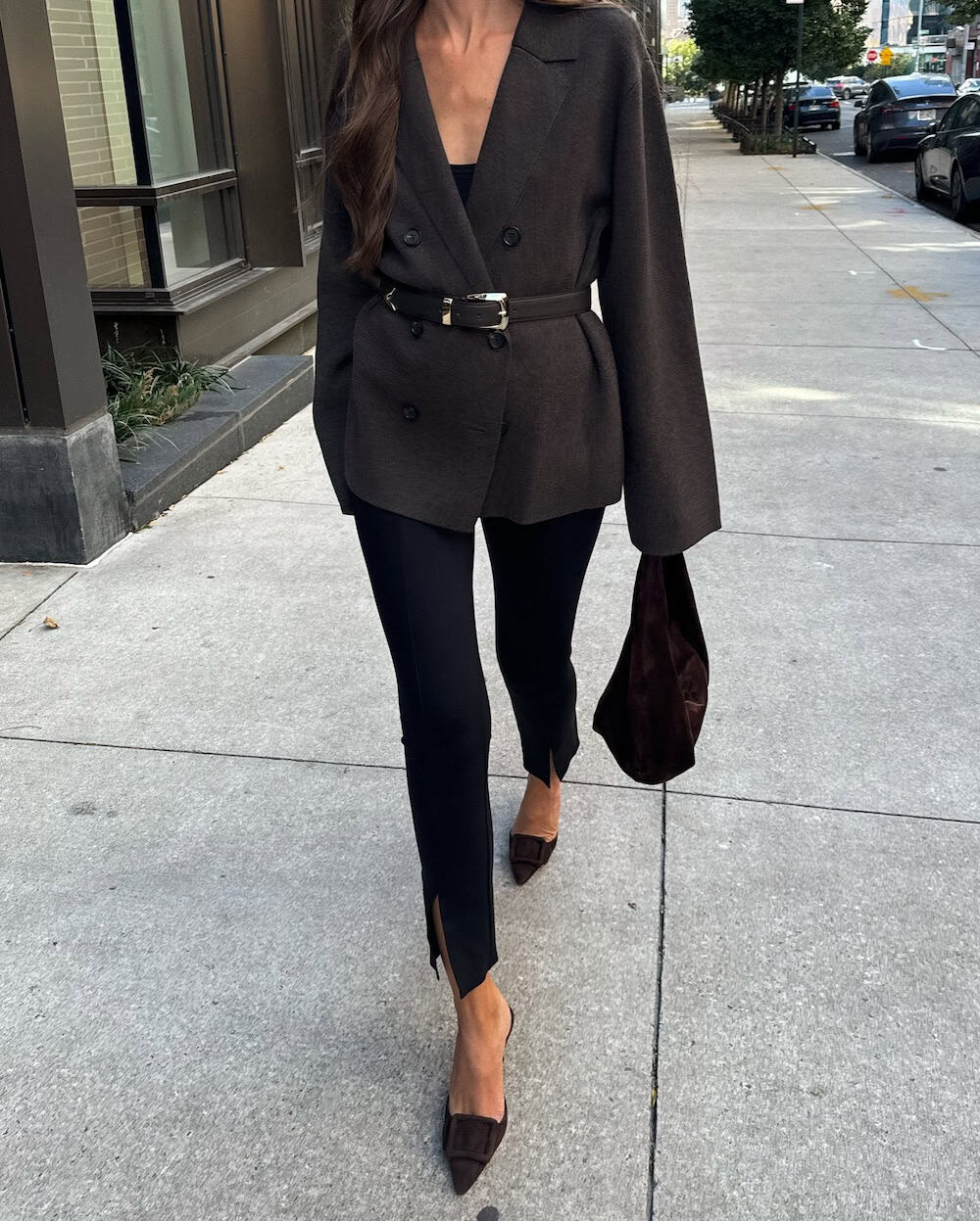 a woman wearing black slacks, a belted blazer, and pointed slide sandals