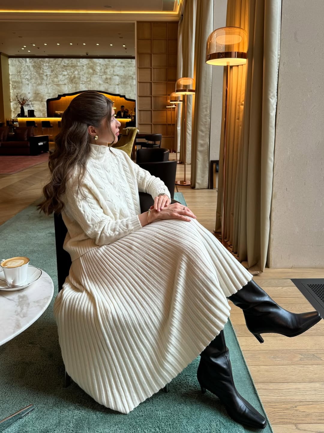 Woman wearing a cream cable-knit turtleneck and skirt with black leather boots.