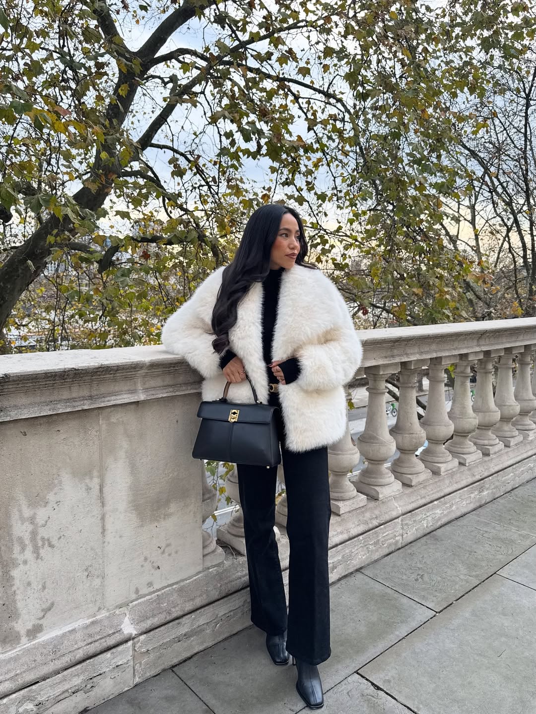 Woman in a white faux fur coat with black trousers and a structured bag.
