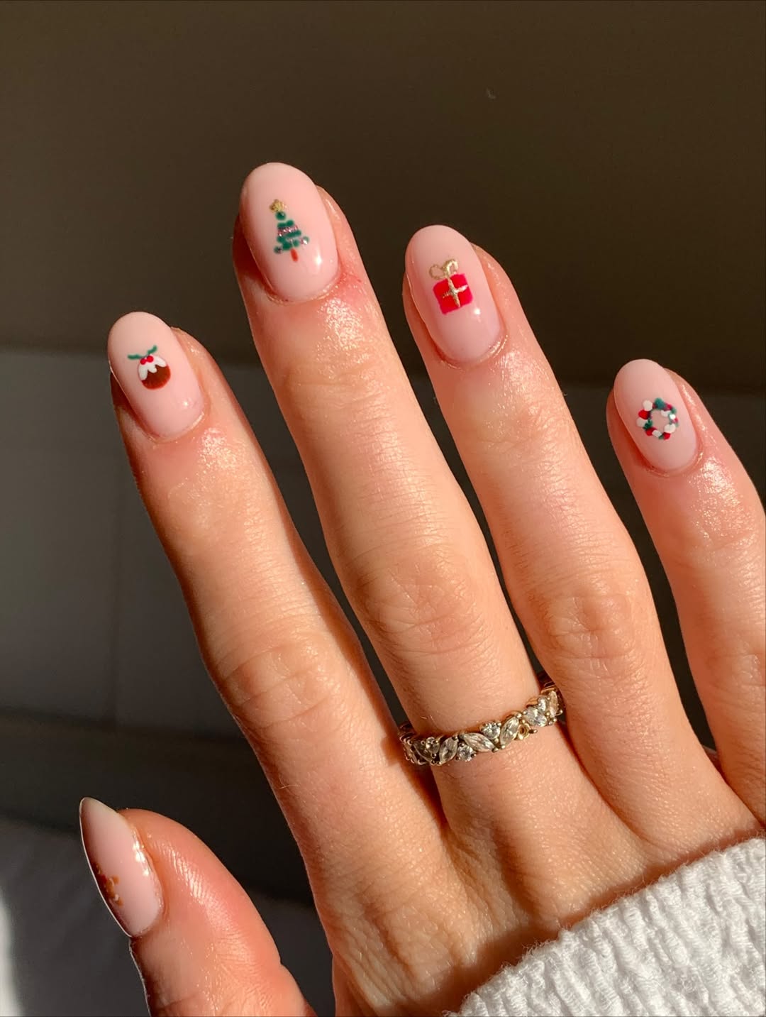 Sheer nude nails adorned with tiny, strategically placed Christmas icons like trees, wreaths, and gifts.