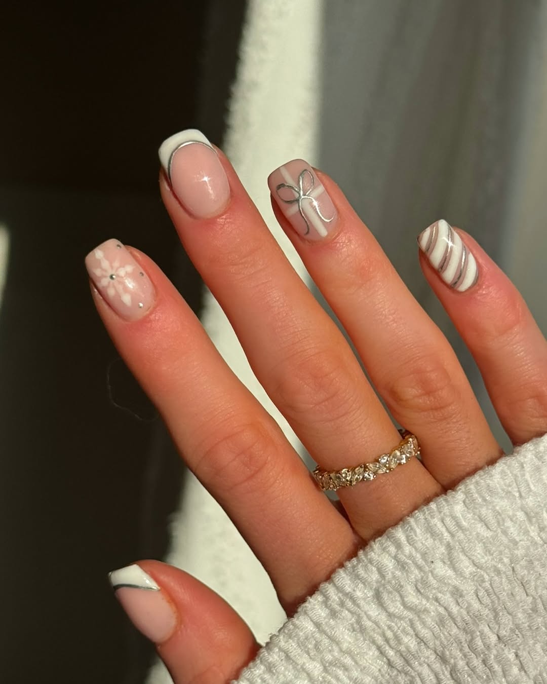 Nude and white nails with silver snowflakes, candy cane stripes, and a bow.