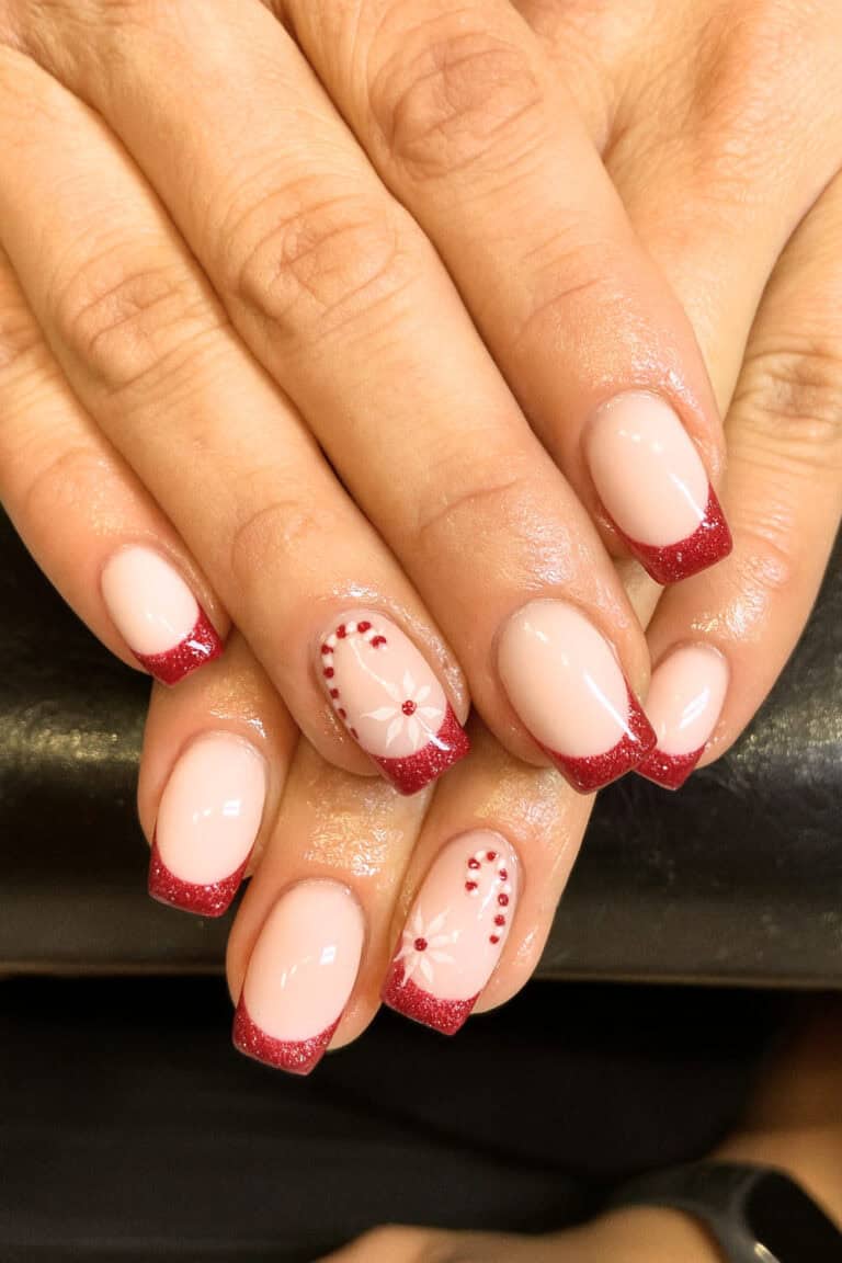Soft pink base with glittery red French tips and subtle floral or candy cane accents.