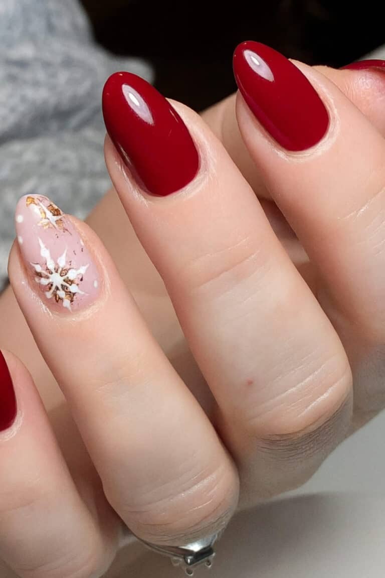 Deep glossy red nails with one accent nail featuring a soft pink base and white snowflake design.