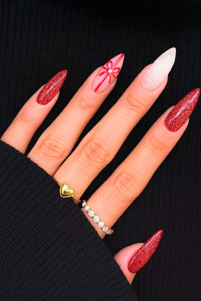 Glittery red stiletto nails with a creamy white accent nail featuring a delicate red bow detail.