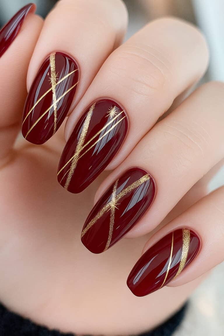 Deep glossy red nails with metallic gold line art and starburst accents