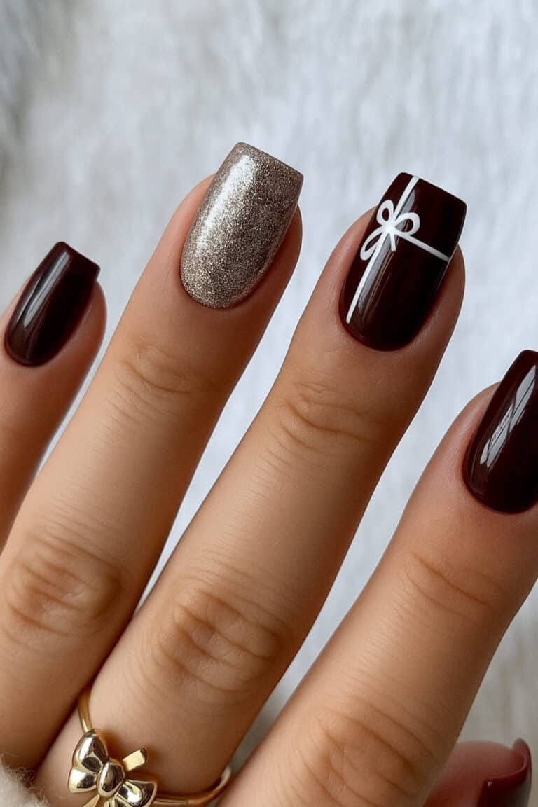 Glossy dark red nails with champagne-gold glitter and a tiny white gift-wrap design