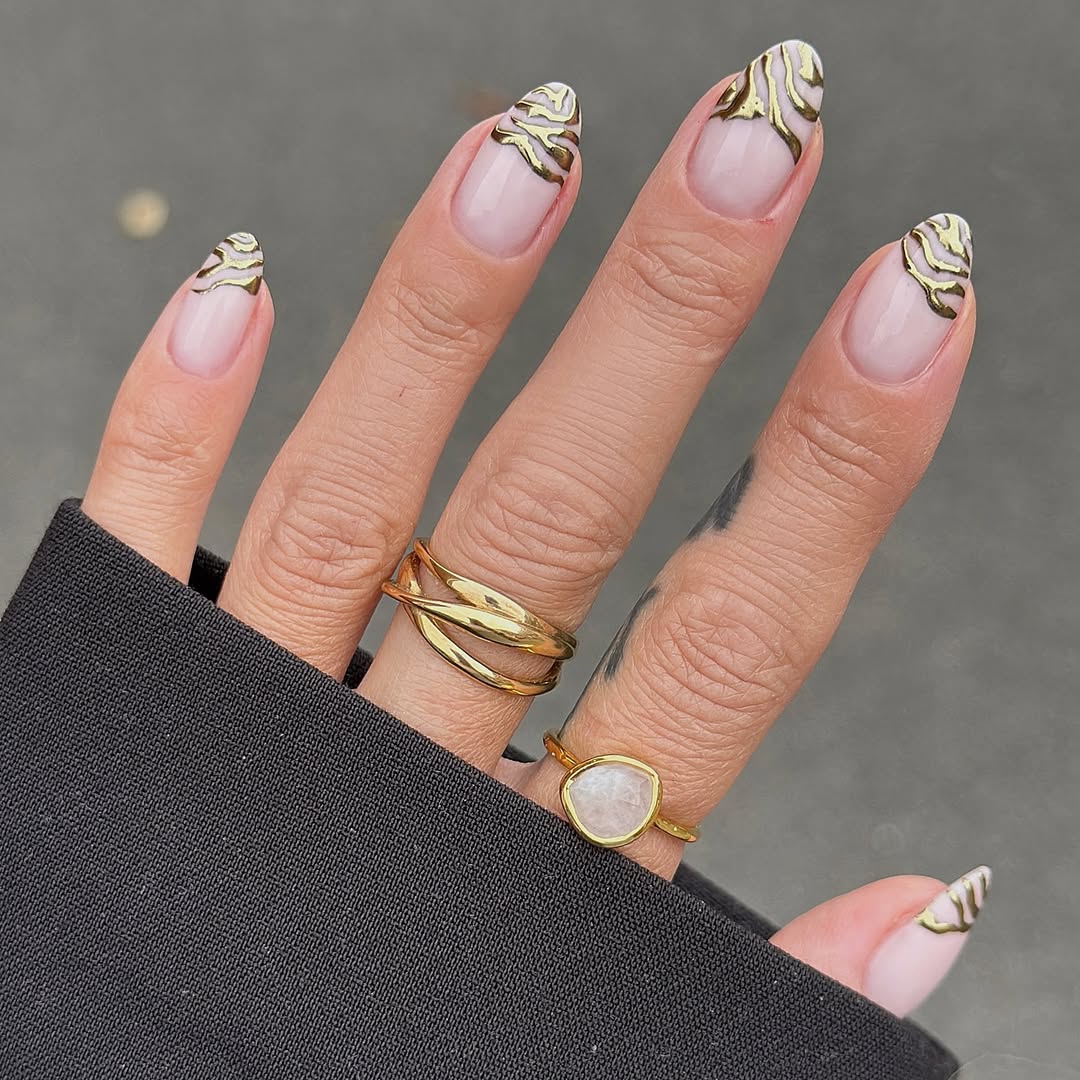 Neutral pink nails with metallic gold swirls decorating the tips.