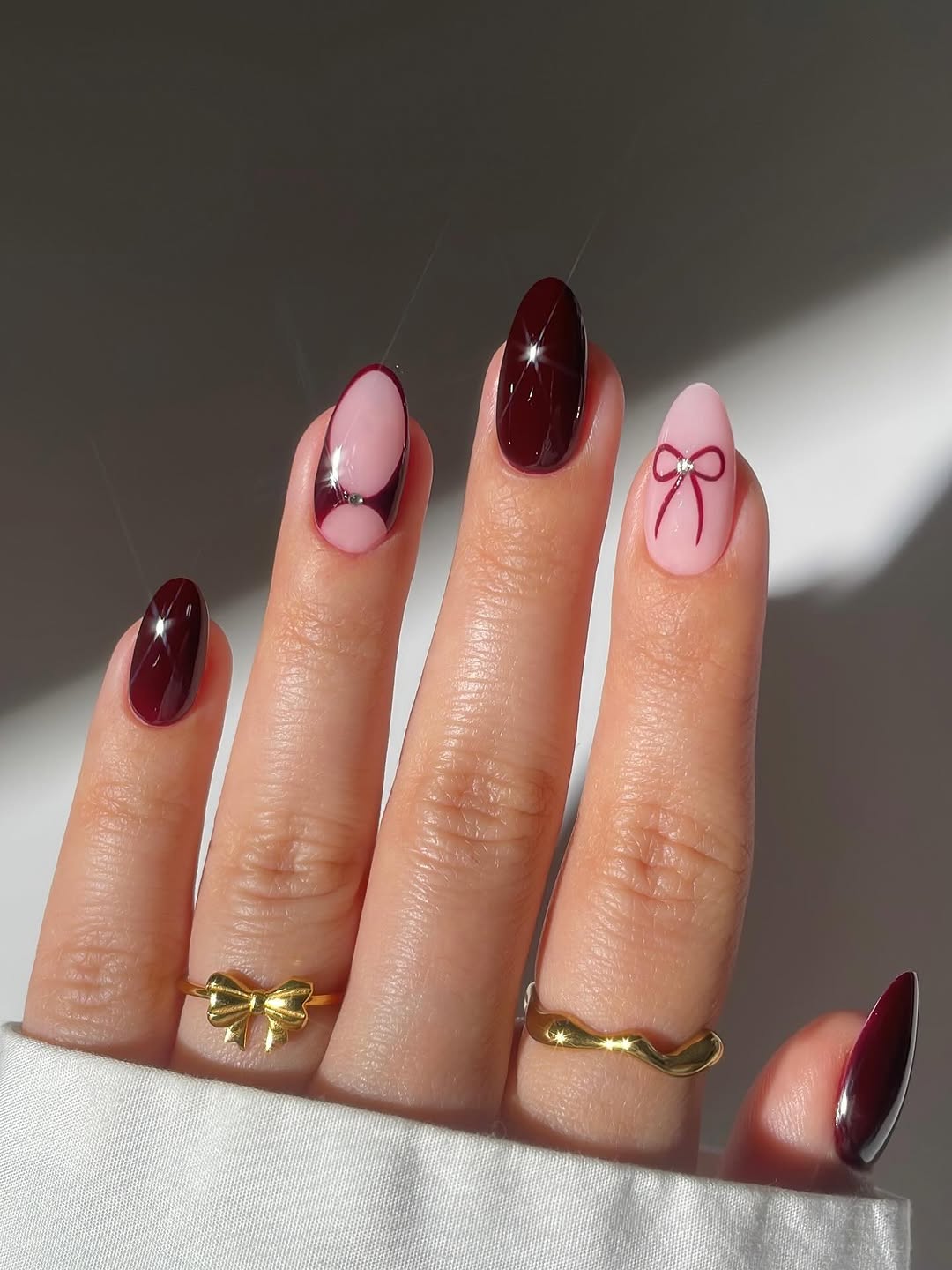 Deep wine-colored nails with nude accents framed by burgundy outlines and a crystal bow detail.