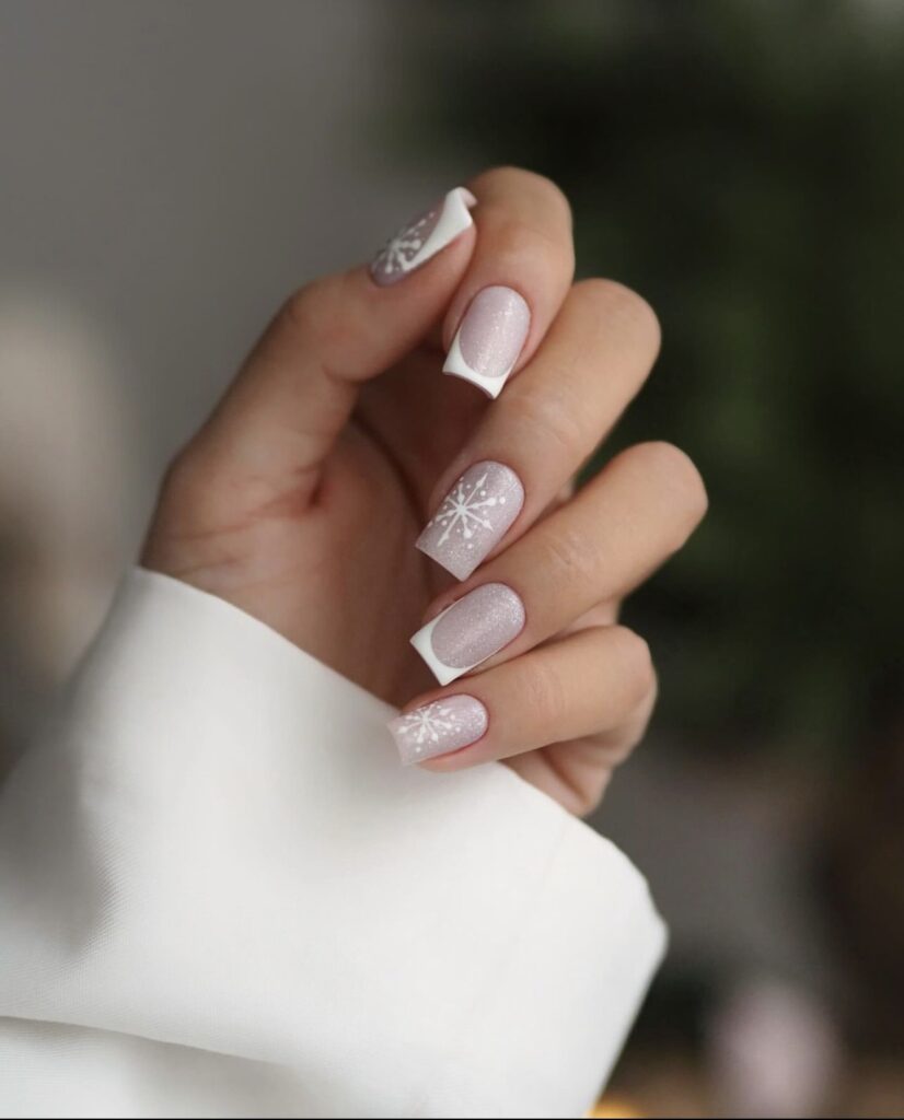 Short winter nails with a light grey base, white snowflake designs, and white French tips.