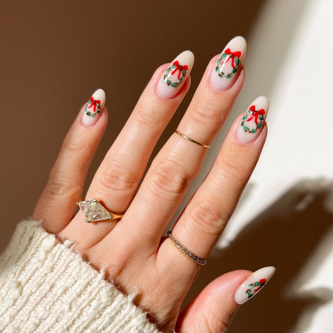 Nude nails featuring hand-painted mini wreaths with green leaves and red bows.