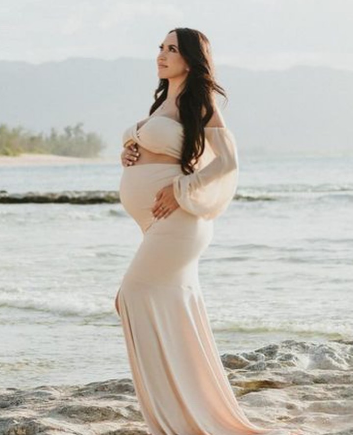 A woman in a flowing, relaxed maternity dress on a beach.