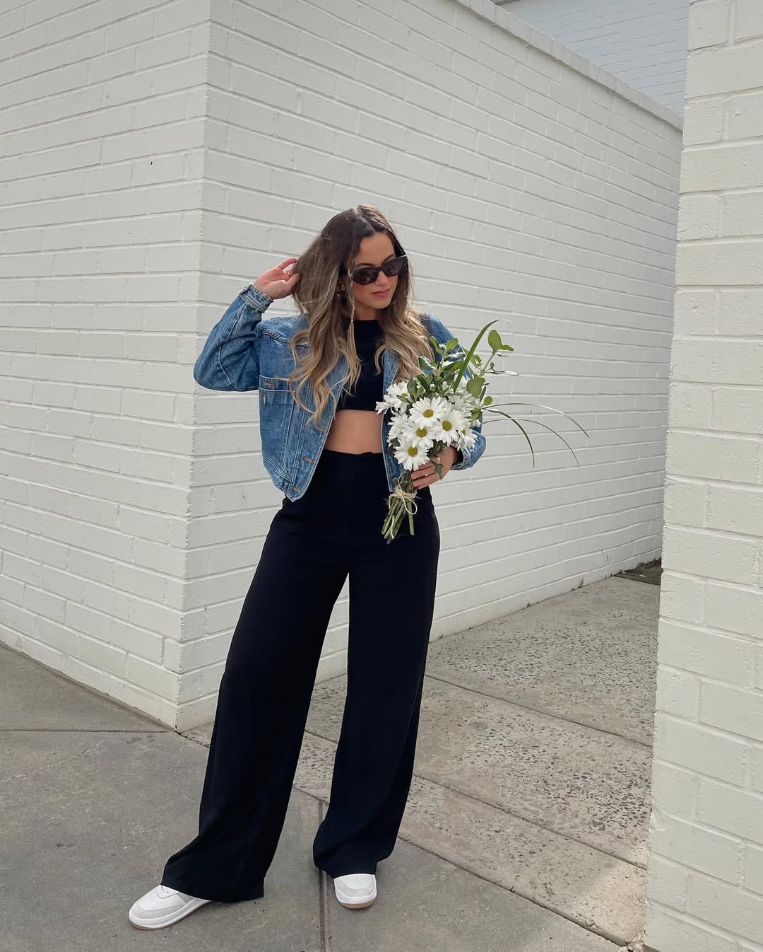 Sleek black layers are softened by a cropped denim jacket and fresh white sneakers, creating a modern and cool aesthetic.