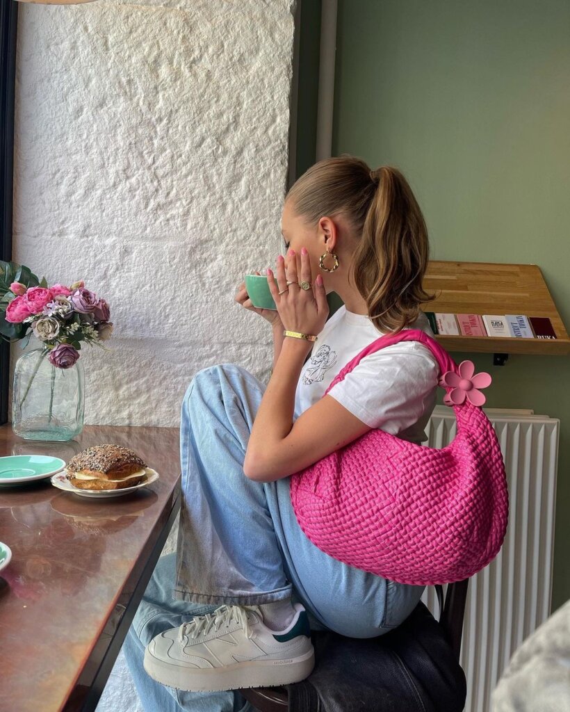 A casual outfit featuring denim and a white tee, highlighted by a vibrant pink handbag, offering a modern and playful aesthetic.