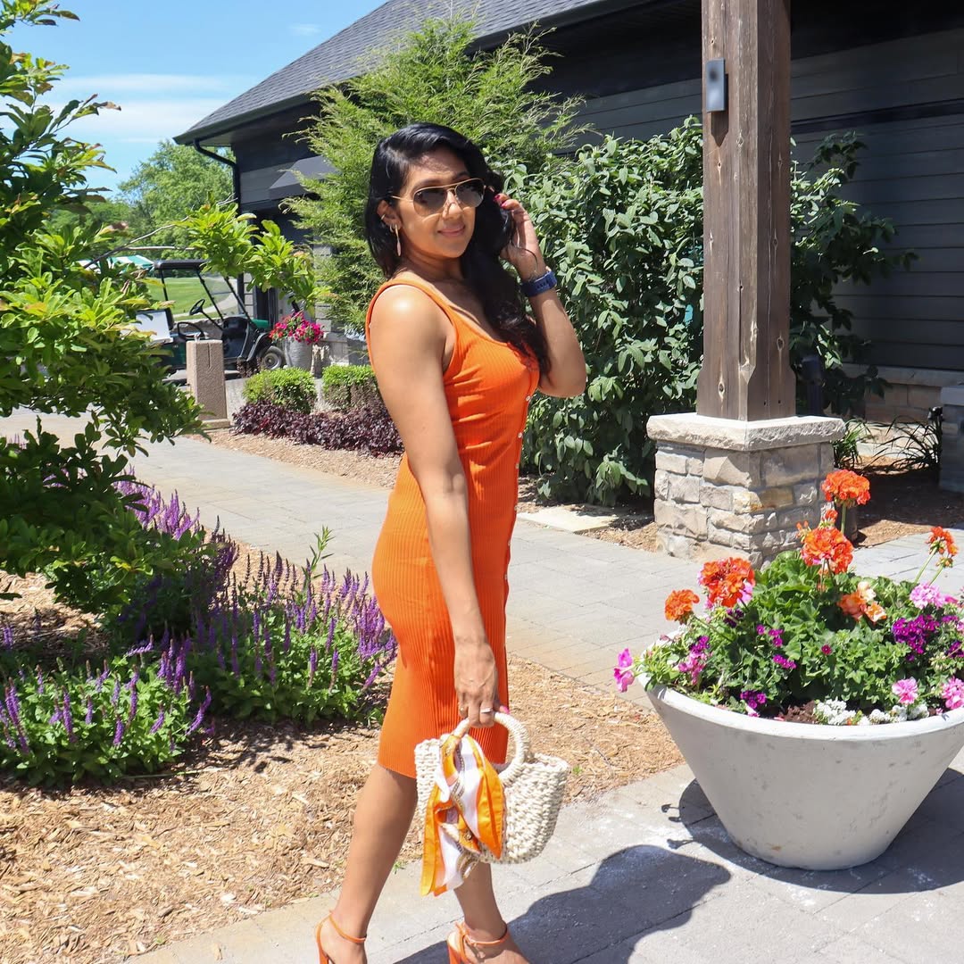 A woman in a vibrant orange dress with a fitted silhouette and straw accessories.