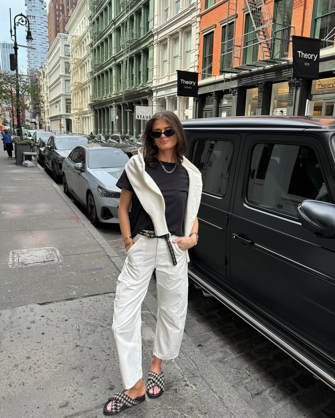Crisp white pants, a black tee, and a sweater draped over the shoulders create a polished yet relaxed city spring look.