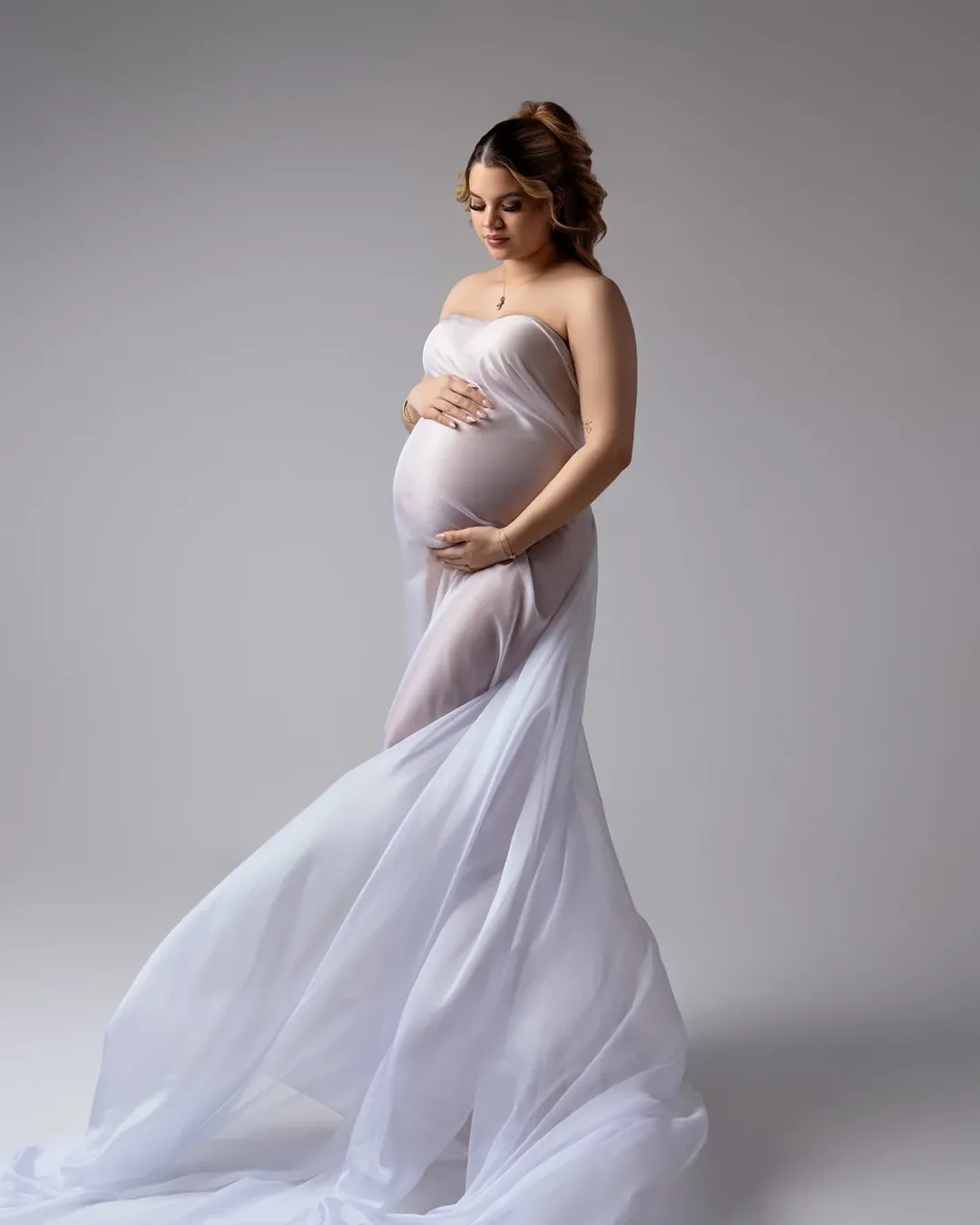 A woman in a simple, light-colored maternity dress in a studio.