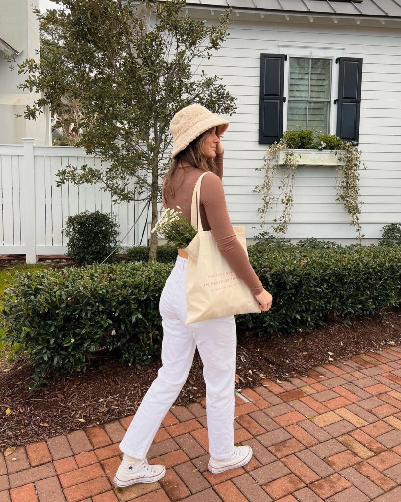 A person in white jeans, a soft brown top, and a canvas tote bag, demonstrating a clean, coastal-inspired spring look.
