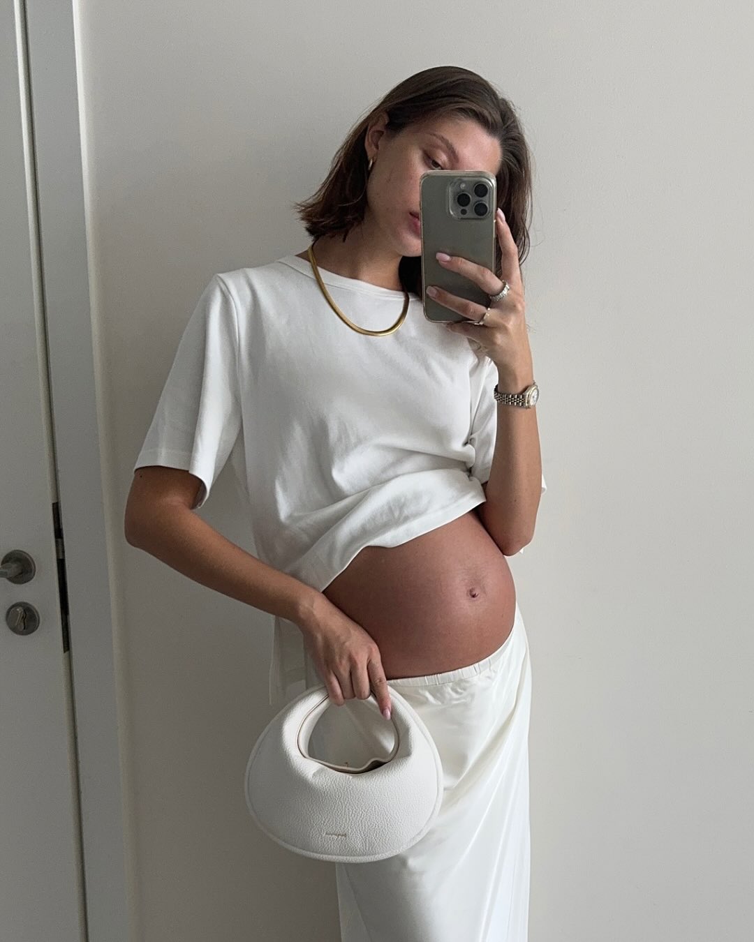 A woman in a white cropped maternity top and flowing white bottoms.