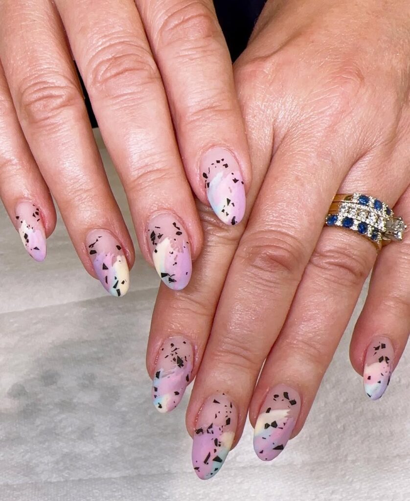 Soft pink nails with black speckles resembling speckled Easter eggs.