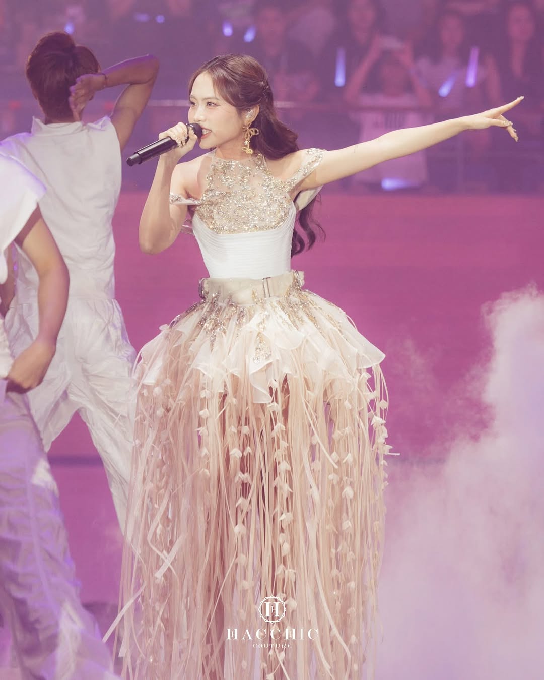 A theatrical festival outfit in soft gold tones with floating fringe and a sculpted bodice, blending couture elegance with concert energy.