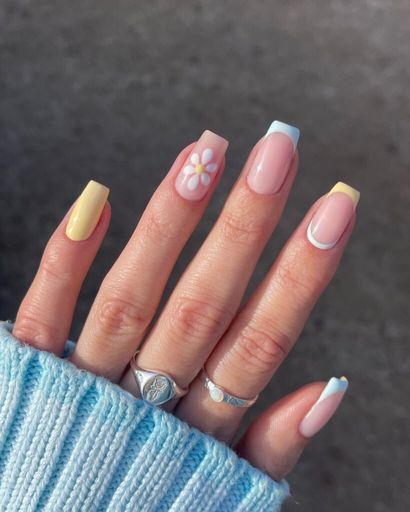 A mix of pastel nails with one accent nail featuring a single daisy.