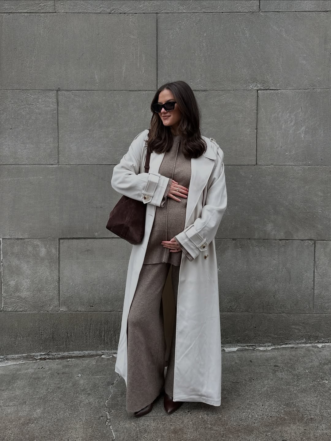 A woman in neutral-toned maternity clothing, including a long coat.