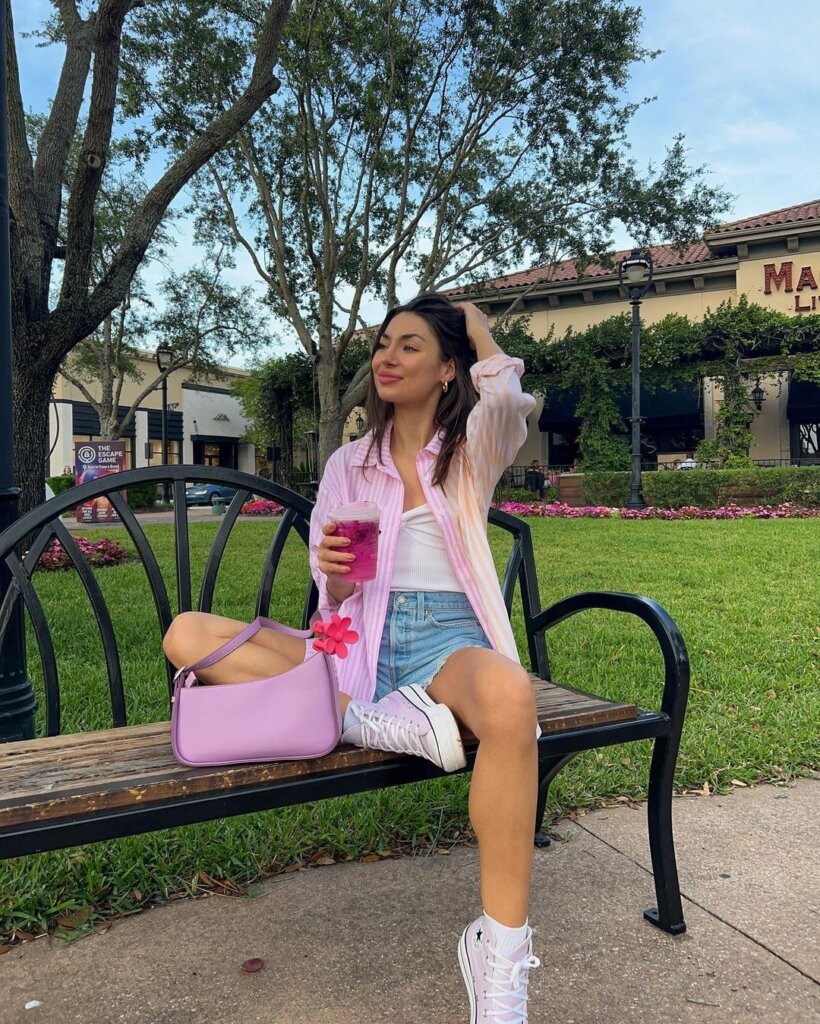 A pink-striped shirt, white top, and denim shorts paired with sneakers and a pastel bag, creating a cheerful and relaxed spring outfit.