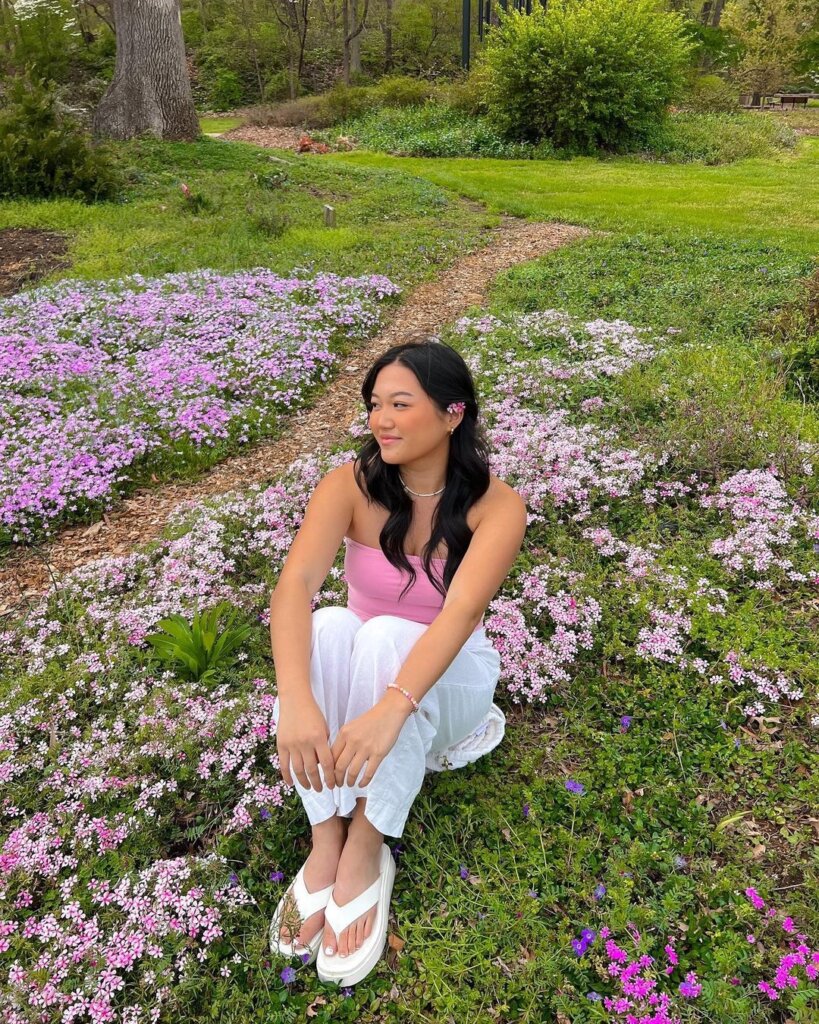 A soft pink top paired with relaxed white pants, set against a floral backdrop, creating a serene and fresh spring look.