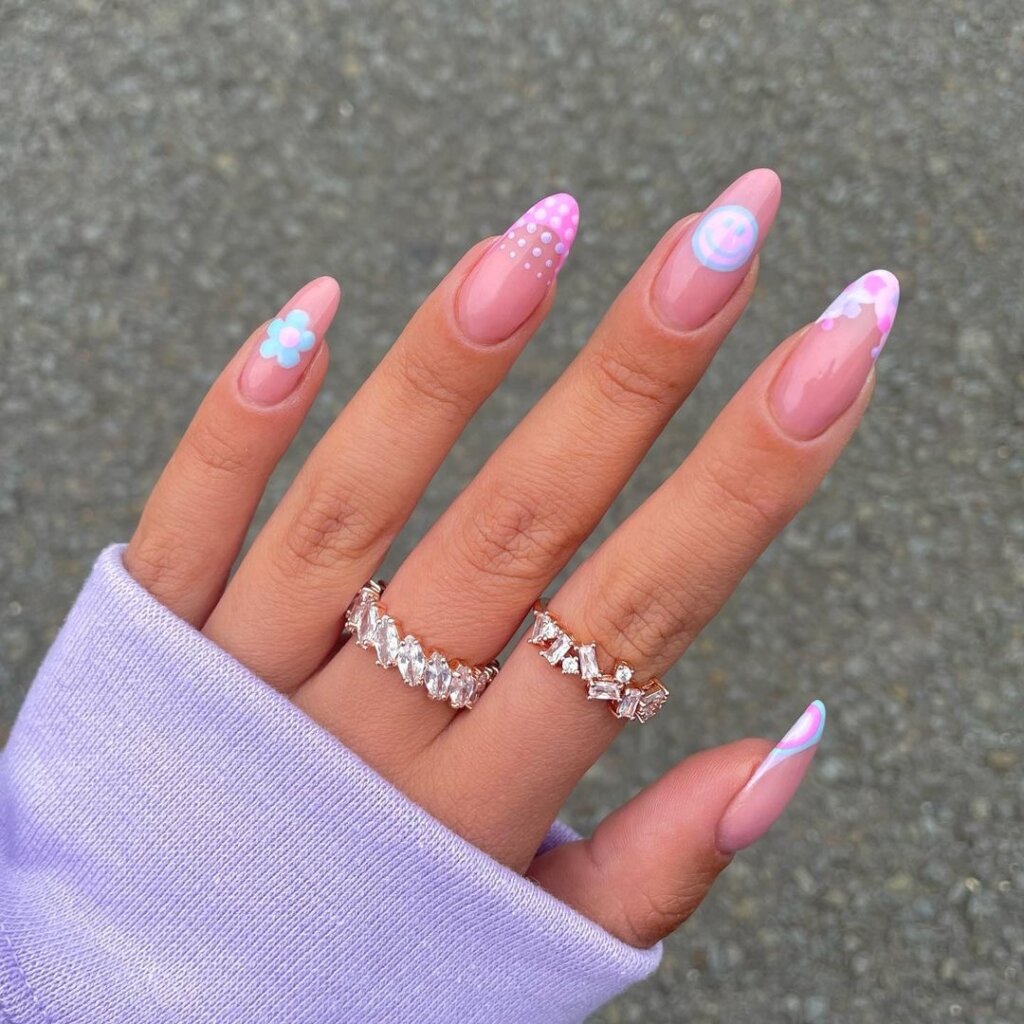 A mix of pastel nails including pink, purple, tiny florals, and a smiley face accent.