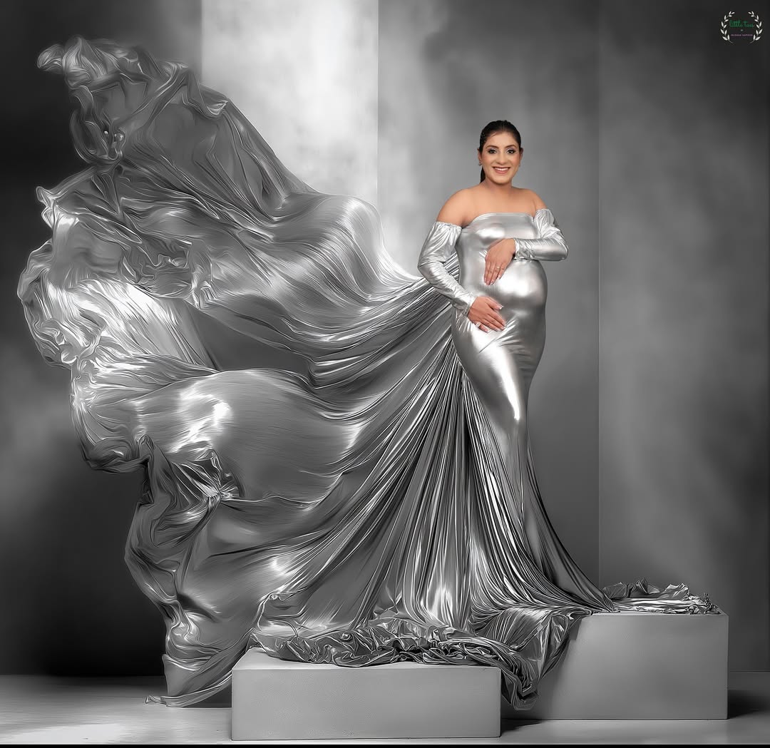 A woman in a shimmering silver, form-fitting maternity gown.