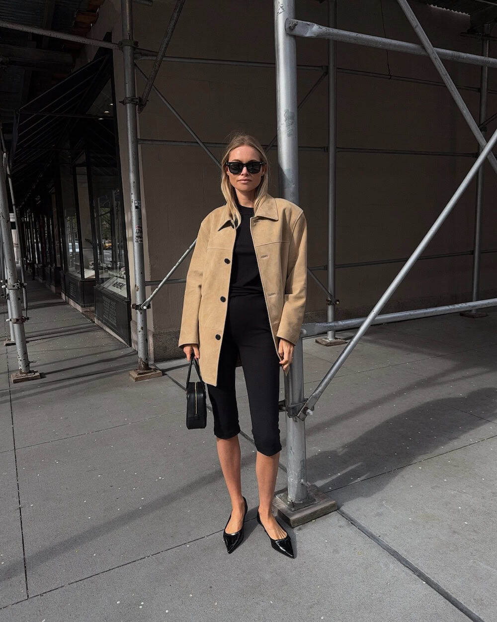 Woman wearing black clothing with a beige suede jacket and pointed ballet flats
