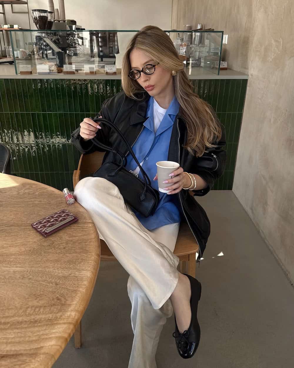 Woman wearing silk pants, a top, and an oversized leather jacket with ballet flats