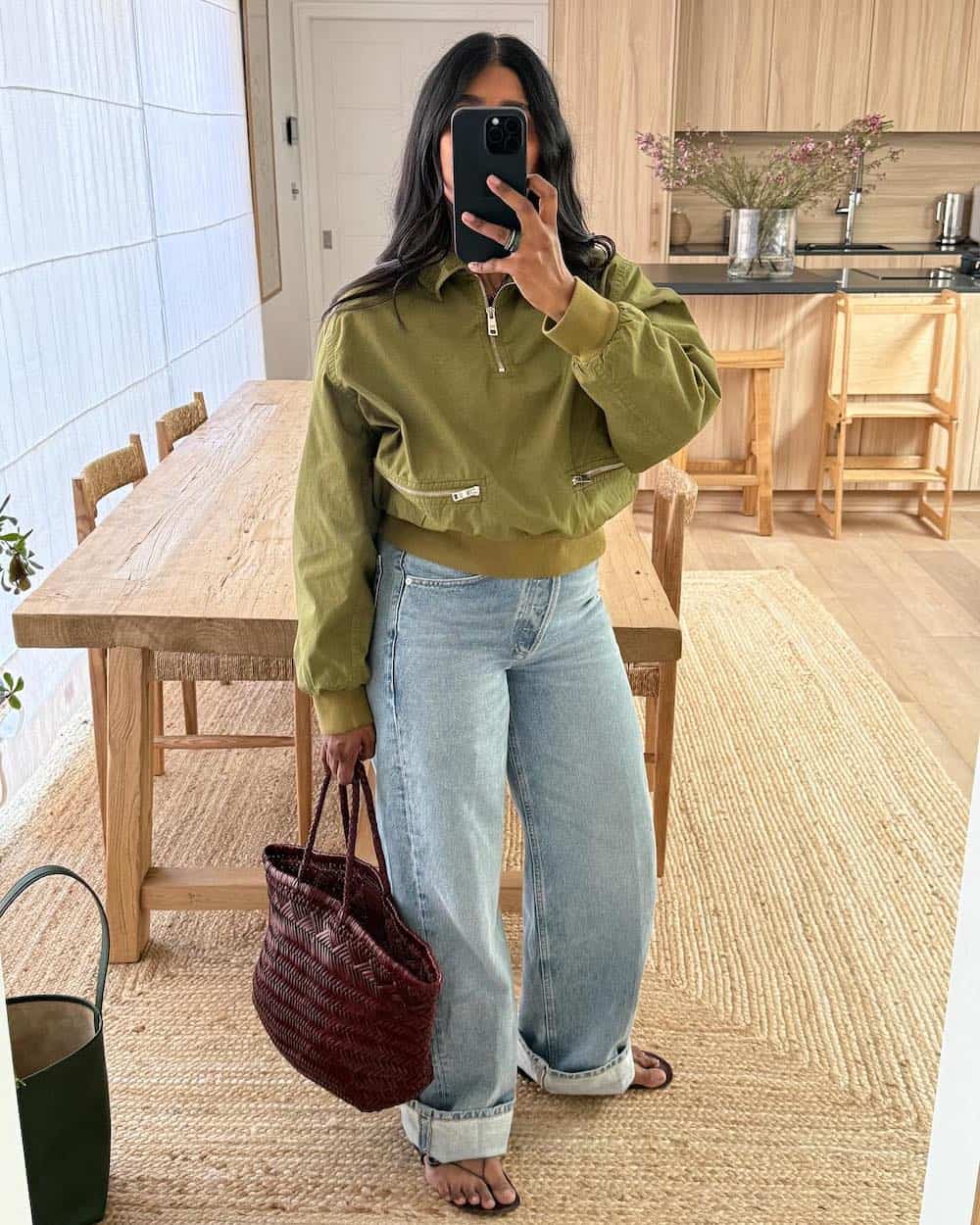 Woman wearing light blue jeans, a cropped green jacket, and sandals