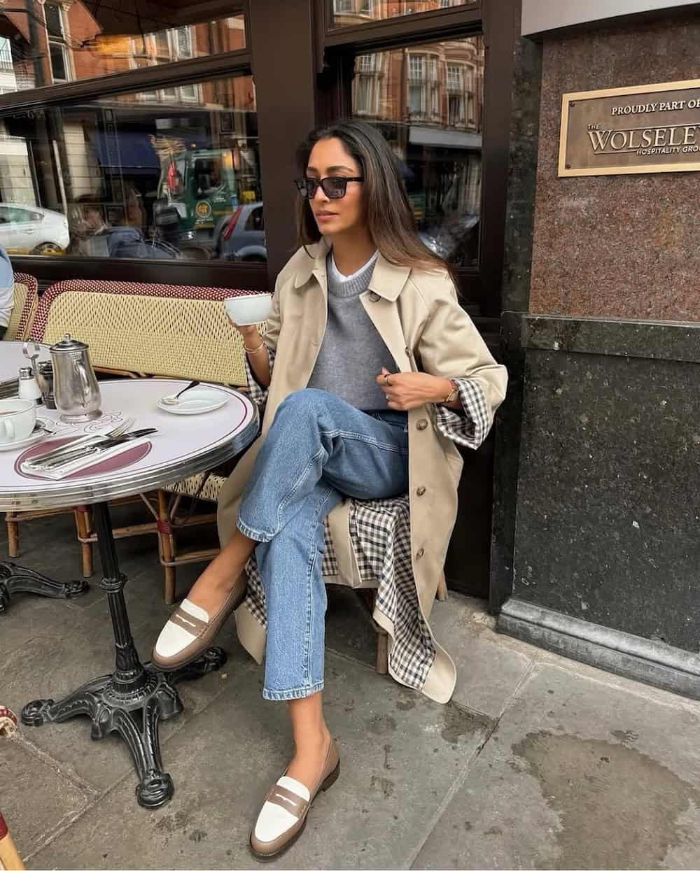 Woman wearing denim, knitwear, a trench coat, and loafers