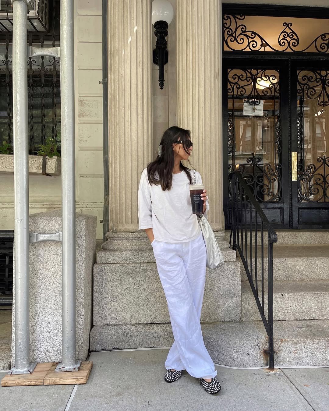 Woman wearing white linen pants with a white boxy tee, black flats, and sunglasses.
