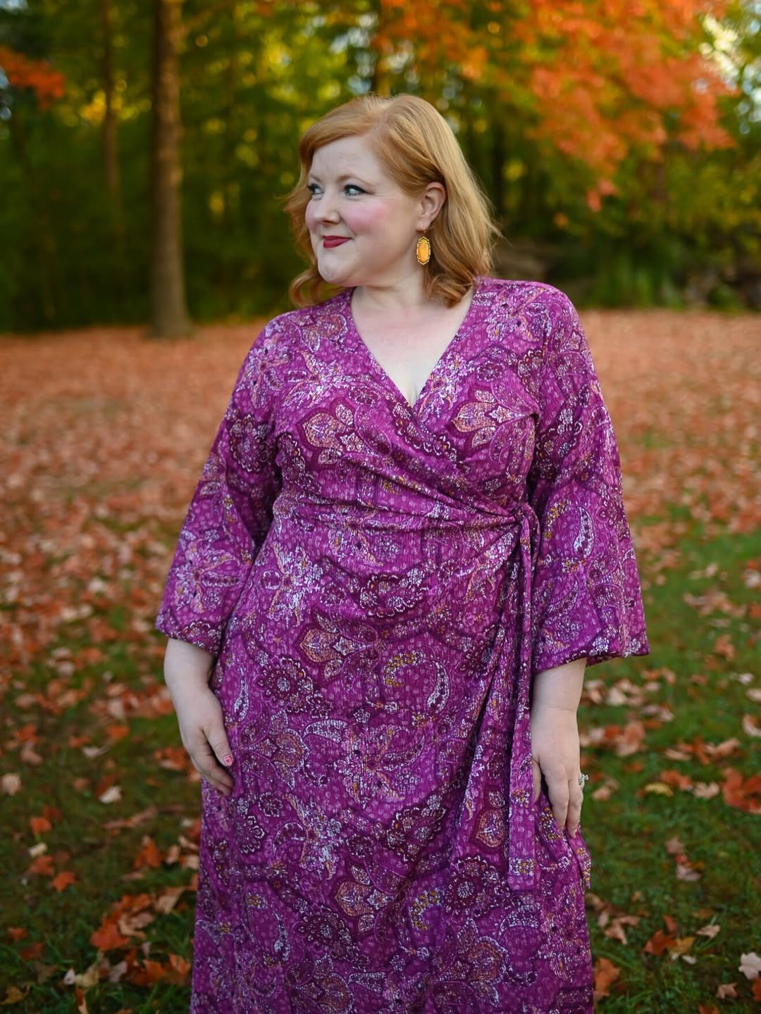 A magenta wrap dress with a paisley print, flattering crossover neckline, and waist tie, set against autumn leaves.