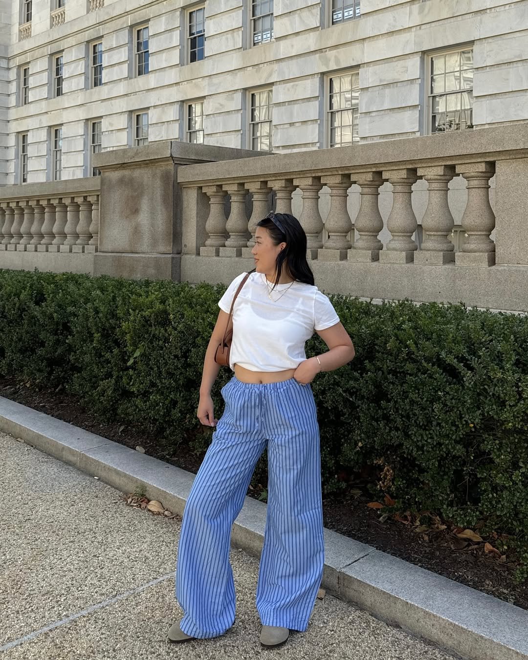 Woman wearing wide blue striped linen pants with a white cropped tee and sunglasses.
