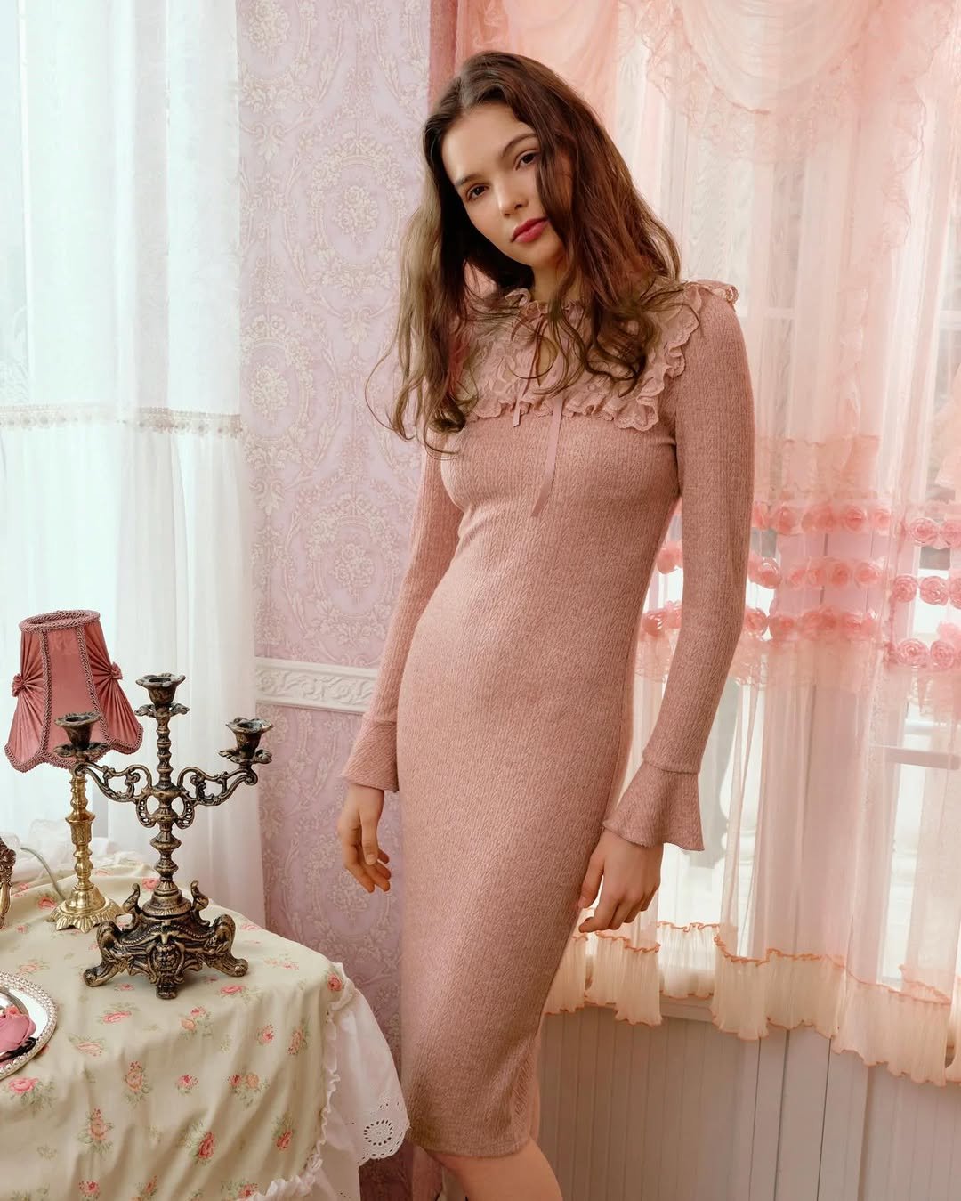 A fitted blush midi dress with a ruffled neckline, styled in a romantic setting.